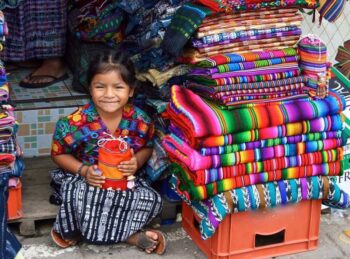 image of girl in colorful clothes next to blankets in market in Guatemala