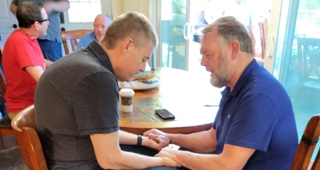 Standing with John Spencer: A Call to Prayer for a Faithful Pilgrimage Leader image of two men, Ken Janke and John Spencer, praying at tabl
