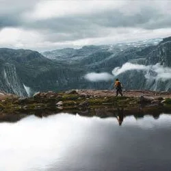 Person hiking between water and mountains in St Olav's Way, Norway