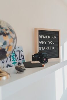 signs says remember why you started with passport, globe, and camera