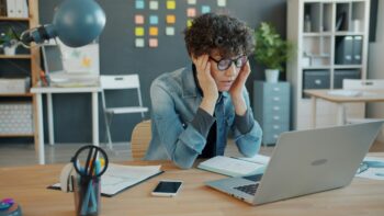 woman with short brown hair and glasses stares at computer and rubs temple for blog about planning a transformational mission trip